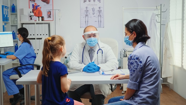 Radioloog met beschermingsmasker die om kinderröntgenstraal vraagt en het controleert. Arts-specialist in geneeskunde die consultatiebehandelingen voor gezondheidszorg verleent in ziekenhuiskast tijdens covid-19