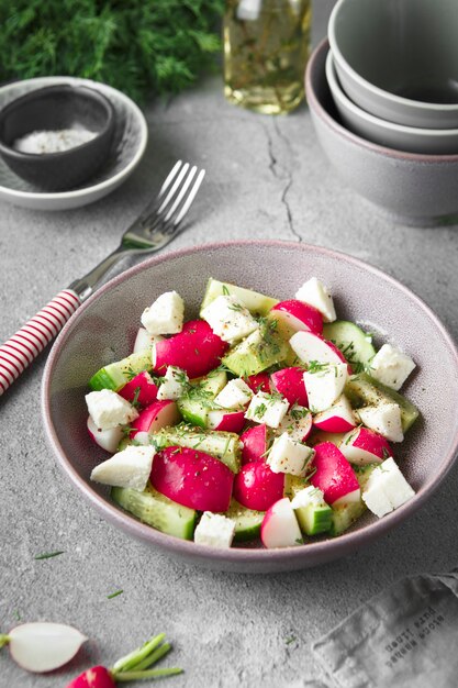 Radish, cucumber, kiwi, cheese and dill salad in a bowl on gray grunge concrete background.