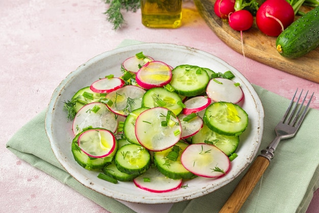 Insalata di ravanelli con cipolla di cetriolo aneto e olio d'oliva in un piatto con forchetta su fondo rosa in cemento da vicino