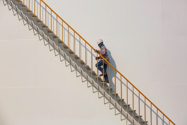 Raffinaderij fabrieksarbeider klimmen metalen trappen op industriële opslagtank olie gebouw.