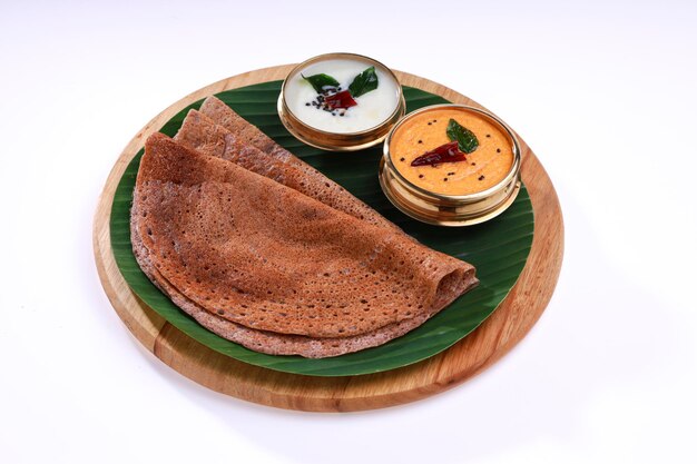 Ragi Dosa, gezond Zuid-Indiaas ontbijtproduct gerangschikt op een ronde houten basis met bananenblad en kokoschutney ernaast.