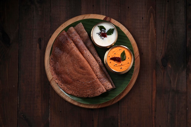 Ragi Dosa, gezond Zuid-Indiaas ontbijtproduct gerangschikt op een ronde houten basis met bananenblad en kokoschutney ernaast.