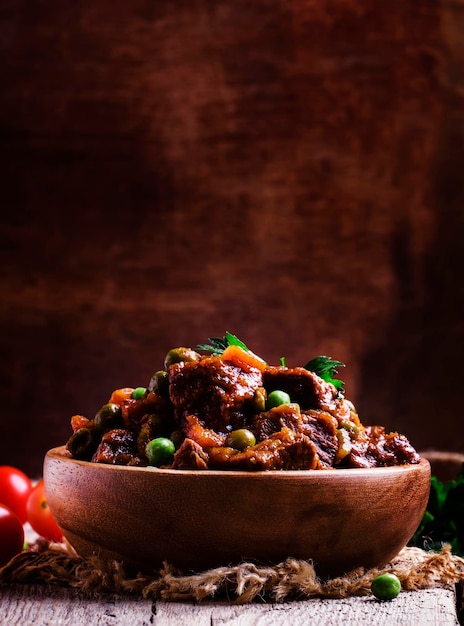 Ragout with beef carrots green peas and tomatoes old wooden background selective focus