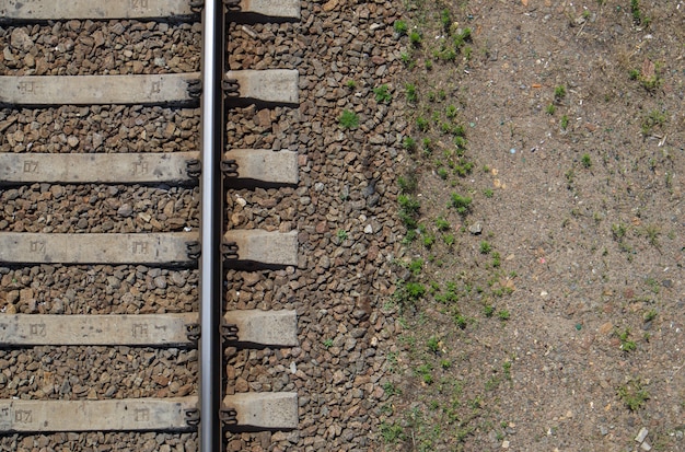 鉄道の上面図、フラットレイ。電車の線路の一部。ドローンからの鉄道の航空写真。テキスト用のスペースのある背景。光沢のある鉄のレールとコンクリート枕木。