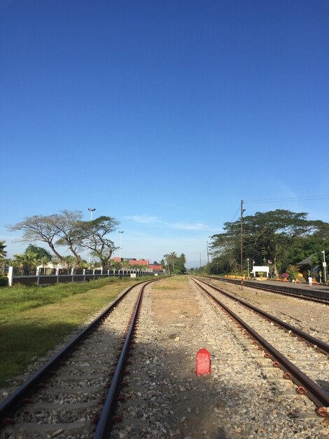 Railroad tracks by trees against clear blue sky