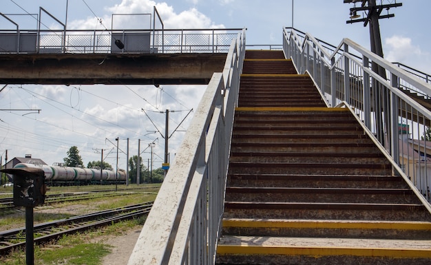 印象的な階段のある階段のある鉄道橋。頭上の横断歩道。駅で1つのプラットフォームを別のプラットフォームに接続する橋の階段。