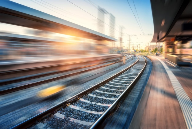 Photo railway station with motion blur effect at sunset industrial landscape with railroad blurred railway platform sky with orange sunlight in the evening railway junction in europe transportation