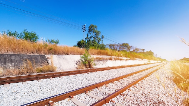 Railway steel twin tracks of train in Thailand with view trees beside road.