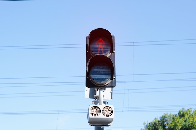 Railway traffic light for pedestrians lit red, indicates Stand, against blue sky outdoors