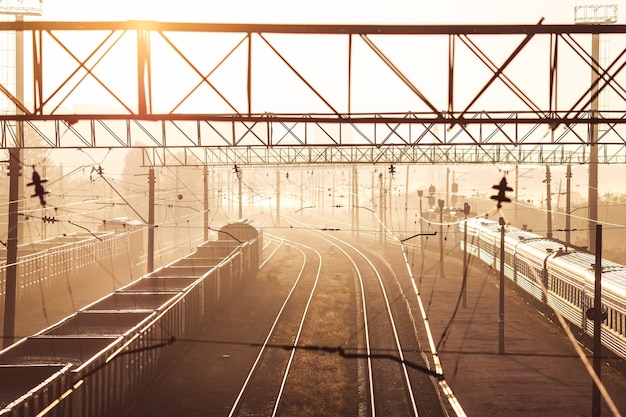 Railway with freight and passenger train at dawn with sun.