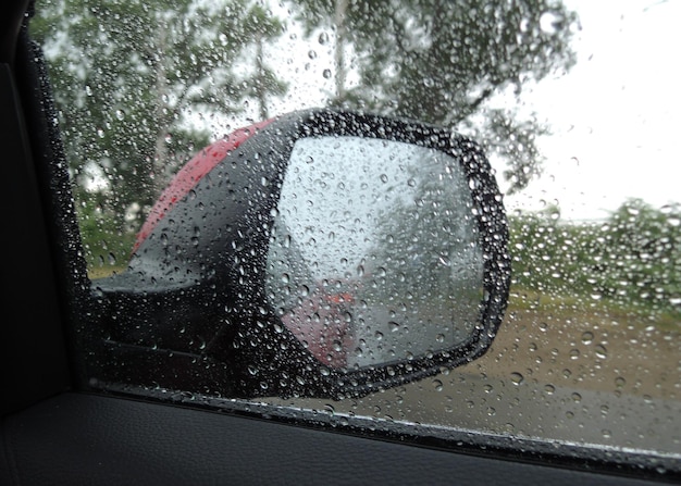 A rain drenched car side window makes it difficult to see in the rearview mirror