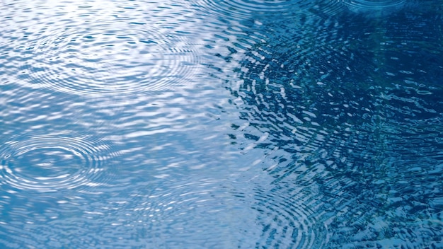 Rain drop falling on swiming pool and ripple shape and sun light reflection on water surface