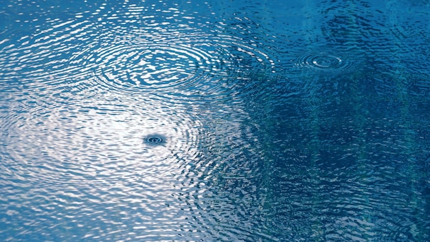 Goccia di pioggia sulla piscina d'acqua e riflesso della luce solare sulla superficie.