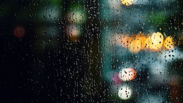 Photo rain drop on window at night. condominium or apartment living room window on rainy season night in bangkok thailand. outside window is blurred bokeh of raining city light and natural tree and sky.