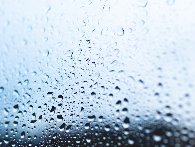 Gocce di pioggia su sfondo di vetro. sagome di gocce d'acqua sulla superficie trasparente blu.