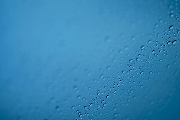 ガラスの上に雨が降ります/青い背景。