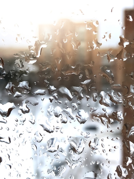 Rain drops on window glass with blurred multi-storey building on background