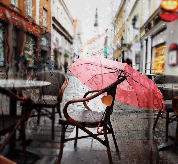 Rain drops and yellow leaves on window view on street with cafe\
table and umbrella in tallinn