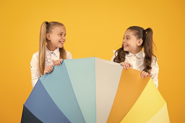 Rain go away little schoolgirls smiling behind bright colored umbrella happy small children walking to school under rain on yellow background it takes sunshine and rain to make a rainbow