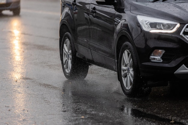 Rain water splash flow from wheels of black car moving fast in daylight city with selective focus