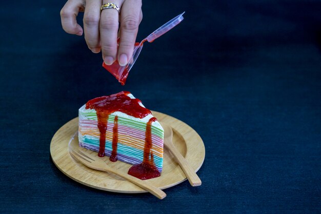 Rainbow crepe cake with strawberry jam on wooden plate