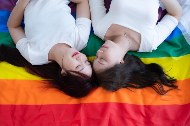 レインボー旗の上でLGBTカップルが幸せに横たわりお互いにしゃべりからかう