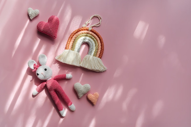 Photo rainbow hearts and knitted bunny on pink background. cute decoration and accessories for baby and children's room. flat lay, top view