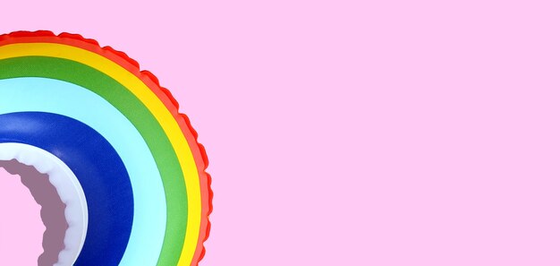 Photo rainbow inflatable swimming pool ring on pink background.