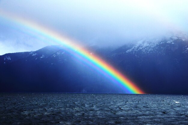 Photo rainbow over lake against mountains and sky