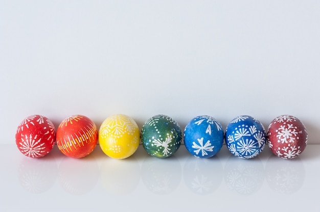 Rainbow line of Easter eggs on white background with reflection. Easter holiday concept. 