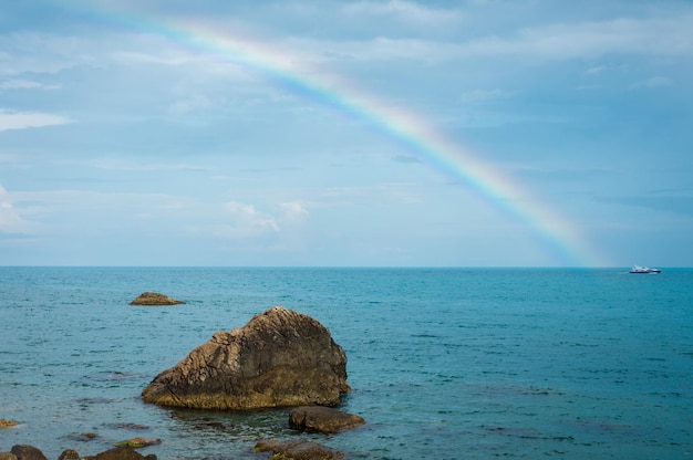 A rainbow over the sea with a large rock in the foreground