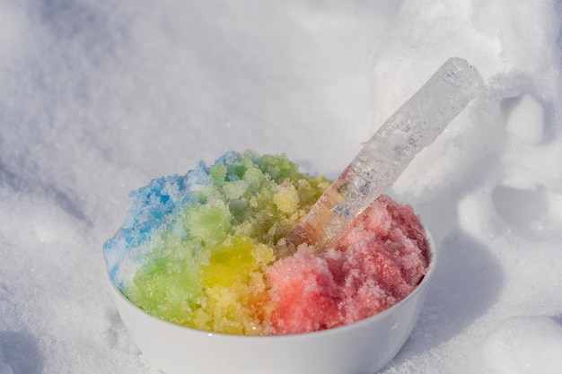Rainbow shaved ice in dessert bowl on white snow background close up