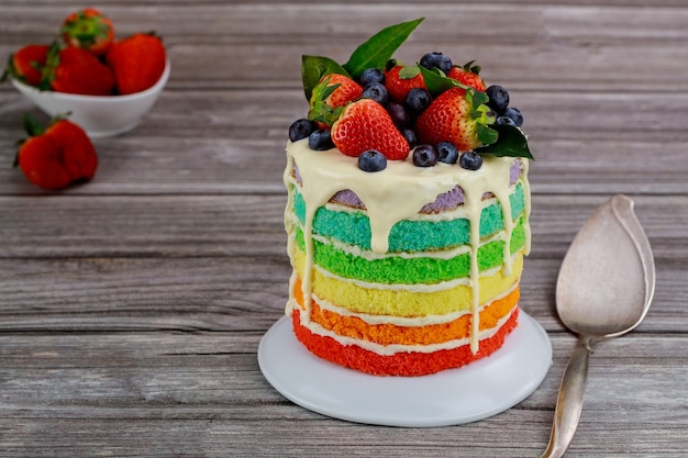 Pan di spagna arcobaleno decorato con frutti di bosco freschi.