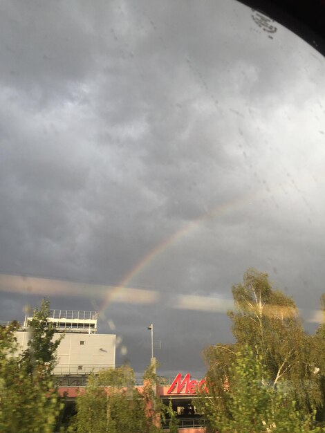 Rainbow over trees against cloudy sky