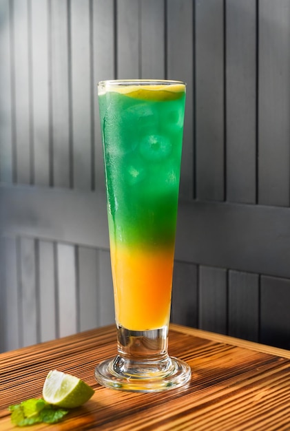 Rainbow yellow green alcohol cocktail on wooden table against dark wall with copy space