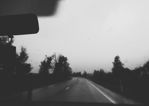 Raindrops on the car window glass. Road and trees. Black and white photo.