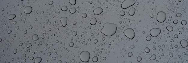 Raindrops on dark glass on rainy day closeup background