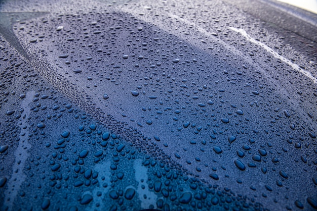 밝은 햇빛에 광택이 나는 자동차의 후드에서 빗방울이 떨어집니다.
