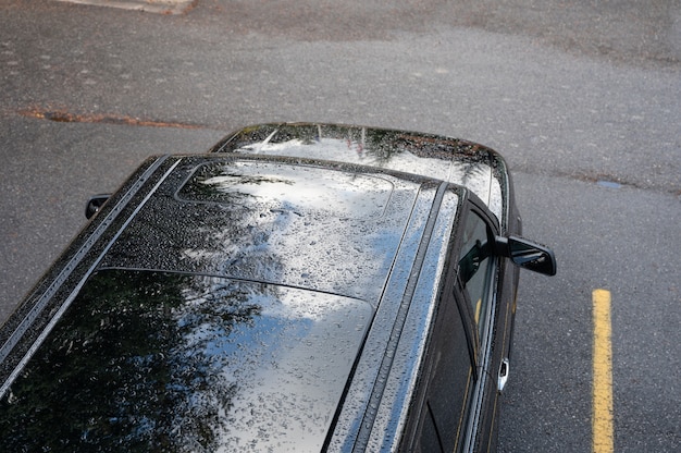 駐車場の黒いSUV車の屋根に落ちる雨滴