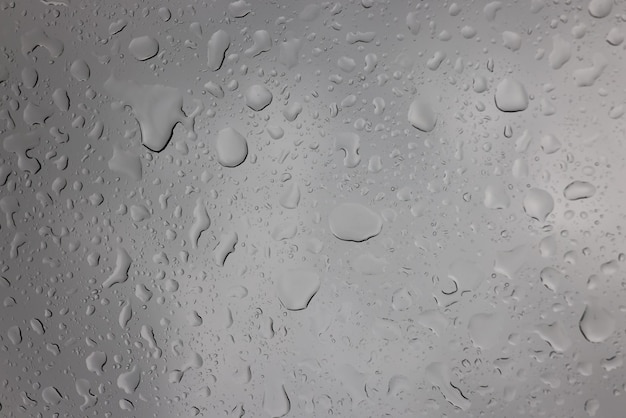 Raindrops on glass against gray sky closeup