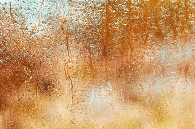 オレンジ色の秋の背景のガラスの雨滴