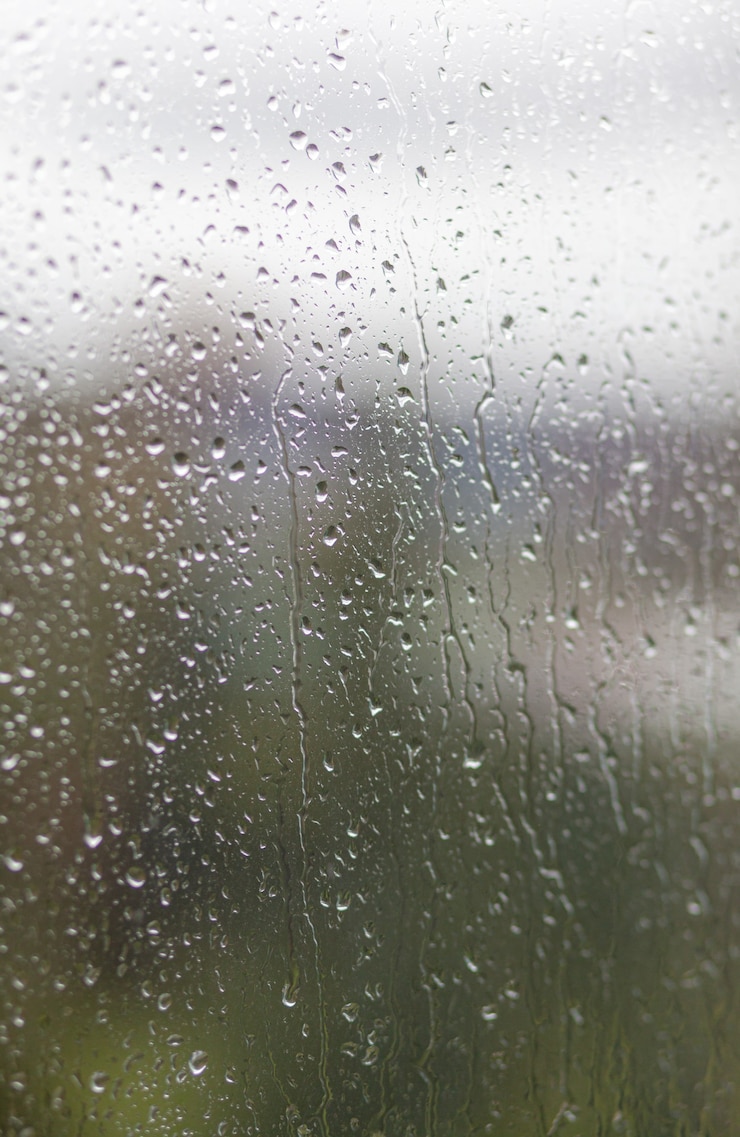 Photo rainy day through the window on cloudy grey sky and city buildings background. concept. evening cityscape behind the glass window with trickling drops of water.