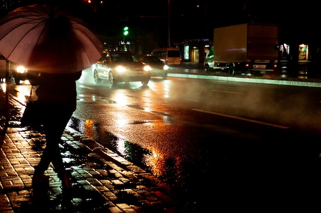 Rainy evening A woman silhouette with umbrella and running traffic with drops of rain Autumn time