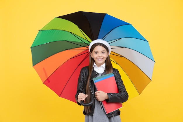 Rainy weather forecast back to school vivid rain protection happy girl in glasses hold notebook education teen child under colorful parasol kid in beret with rainbow umbrella autumn season