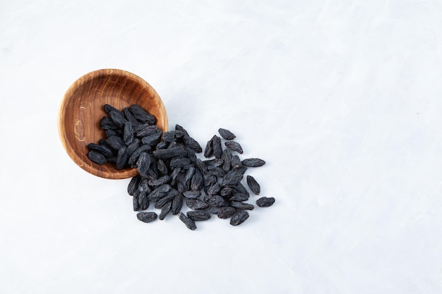 Raisins from dark grapes spilled out of wooden bowl onto gray surface Selective focus copy space