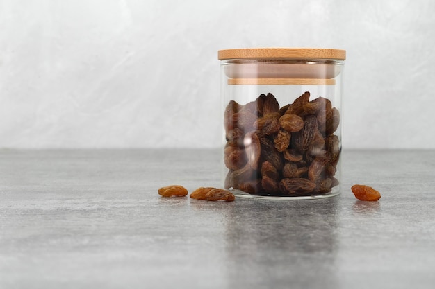 Raisins in glass jar on stone texture background Dry raisins Bulk raisins grains