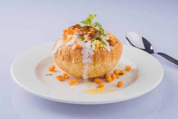 Rajasthani Shahi Raj Kachori, stuffed with potato and sprout filling. served with curd, chutney and sev in a plate, isolated over colourful or wooden background. selective focus