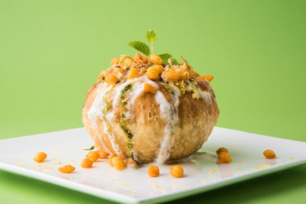 Rajasthani Shahi Raj Kachori, stuffed with potato and sprout filling. served with curd, chutney and sev in a plate, isolated over colourful or wooden background. selective focus
