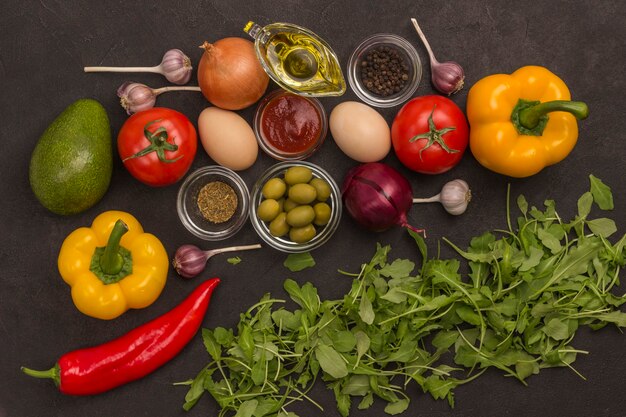 Raket en spinazie, eieren en tomaten, paprika, knoflook, olijven op zwarte achtergrond