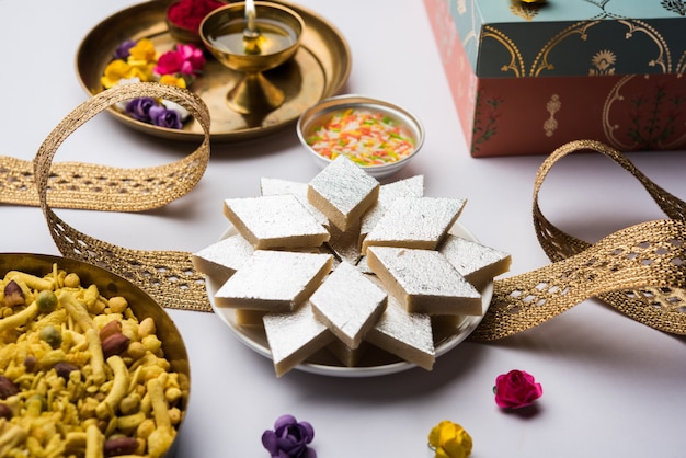 Raksha bandhan festival saluti: rakhi concettuale realizzato utilizzando un piatto pieno di kaju katli barfi o burfi e banda di fantasia e pooja thali. messa a fuoco selettiva
